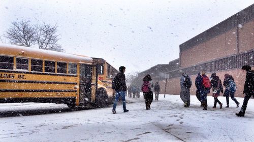 Students walking towards school building while snowing