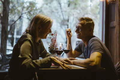 Happy man flirting with woman while sitting with wineglasses on table during date at bar