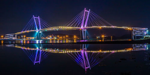 Illuminated bridge over river against sky at night