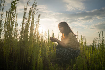 Woman sitting on field against sky during sunset