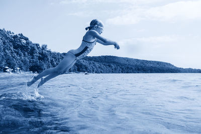 Full length of girl diving in sea against sky