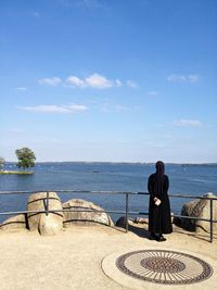 Rear view of a nun overlooking calm blue sea