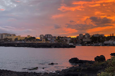 Sea and buildings against sky during sunset