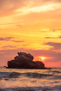 Rock formation in sea against sky during sunset