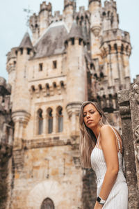 Young woman looking away while standing against historic building