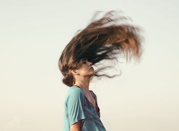 Young woman tossing brown hair against clear sky