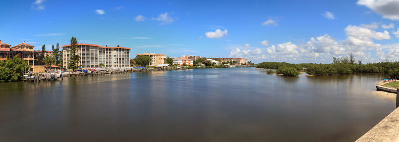 Buildings by river against blue sky