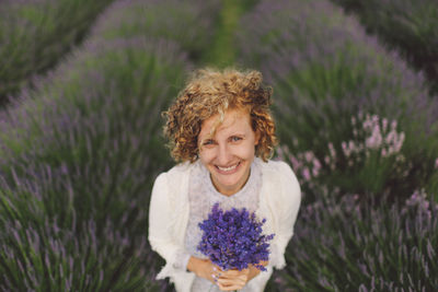 Portrait of cheerful woman holding lavender flowers on field