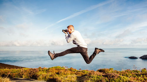 Full length of young man jumping in sea against sky