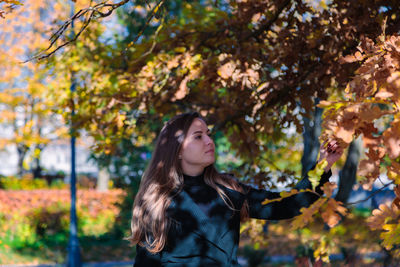 A woman with long hair looks at yellow leaves in an autumn park. autumn season. person