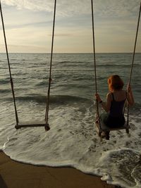 Rear view of woman sitting on beach against sky during sunset