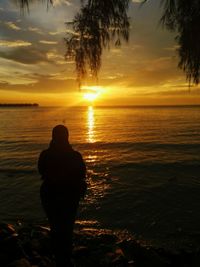 Silhouette of man looking at sea during sunset