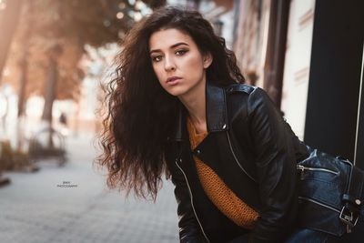 Portrait of beautiful young woman sitting on footpath