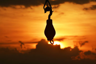 Close-up of silhouette person holding hanging against sky during sunset