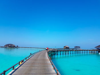 Pier over sea against clear blue sky