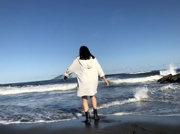 Rear view of woman standing on beach against clear sky