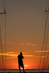 Silhouette man standing by sea against sky during sunset