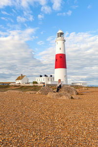 Woman sitting on rock against lighthouse