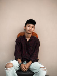 Portrait of young man sitting against wall