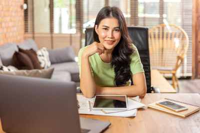 Portrait of young woman using phone while sitting on table