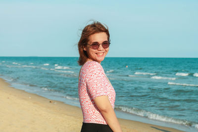 Portrait of young woman standing at beach against clear sky