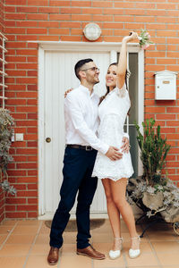Full length of couple standing against brick wall