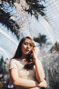 Low angle portrait of young woman standing by plants in park