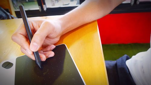 Cropped hand of man writing on graphics tablet at desk