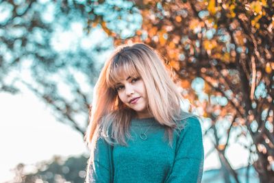 Portrait of smiling young woman standing against tree during autumn