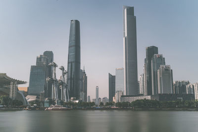 Modern buildings by river against clear sky