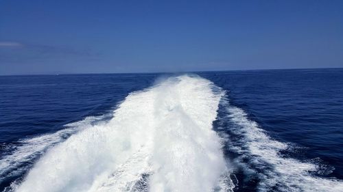 Waves splashing on sea against clear blue sky