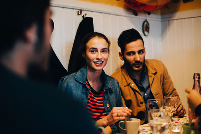 Young man and woman looking at male friend during dinner party at restaurant