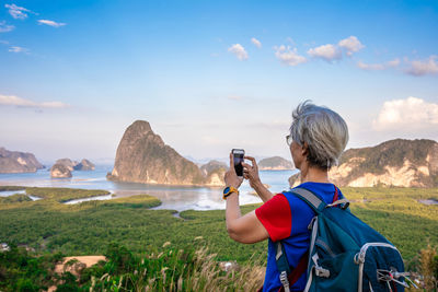 Rear view of woman photographing on mountain against sky