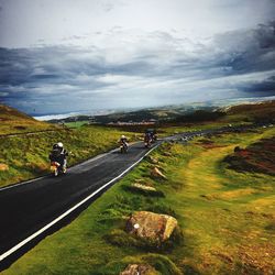 Rear view of people riding motorcycle on road against cloudy sky