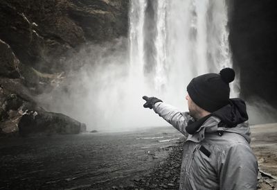 Man pointing at waterfall falling from mountain