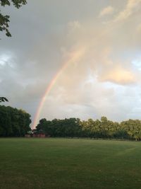 Rainbow over field against cloudy sky