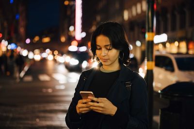 Young woman using mobile phone while standing in city at night