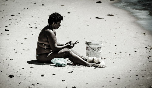 Full length of shirtless man using mobile phone on beach
