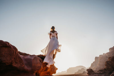 Woman in dress standing on rock against sky
