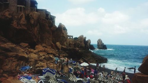 People on rock by sea against sky