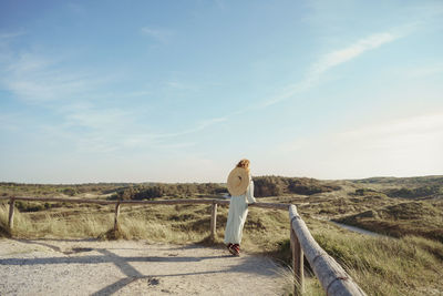 Rear view of woman walking on field against sky