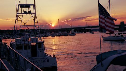 Sailboats moored on harbor in city against sky during sunset