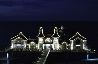 Illuminated building by sea against sky at night