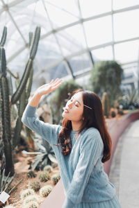 Young woman with eyes closed standing against plants in greenhouse