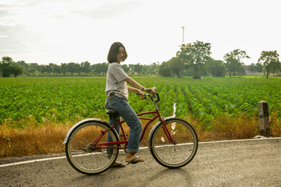 Side view of a young woman riding bicycle on field