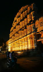 Man riding motorcycle on illuminated street by buildings at night