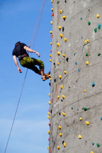 Low angle view of man climbing wall against sky