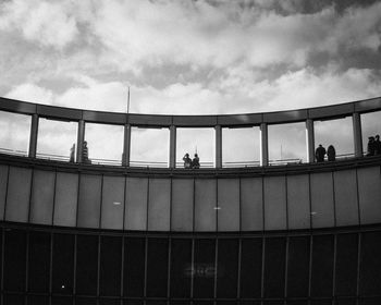 Low angle view of people standing on railing against sky