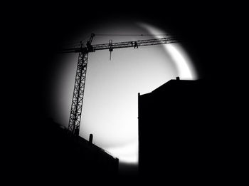 Low angle view of silhouette crane by building against clear sky