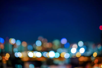 Defocused image of illuminated cityscape against blue sky